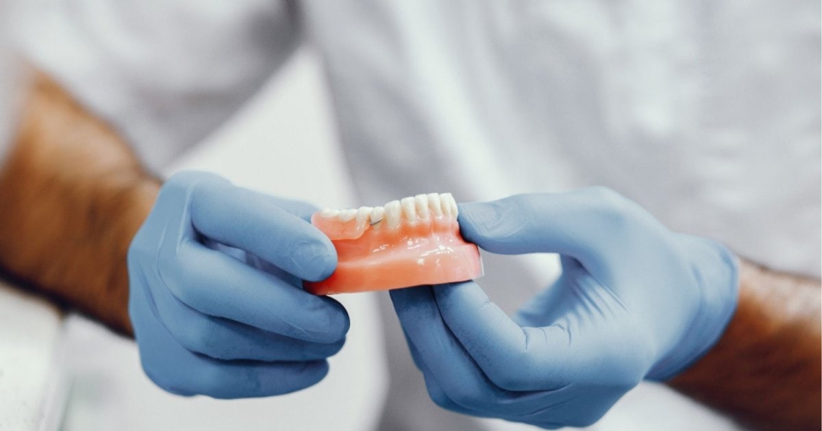 dentist in gloves holding and inspecting a denture in Cardiff