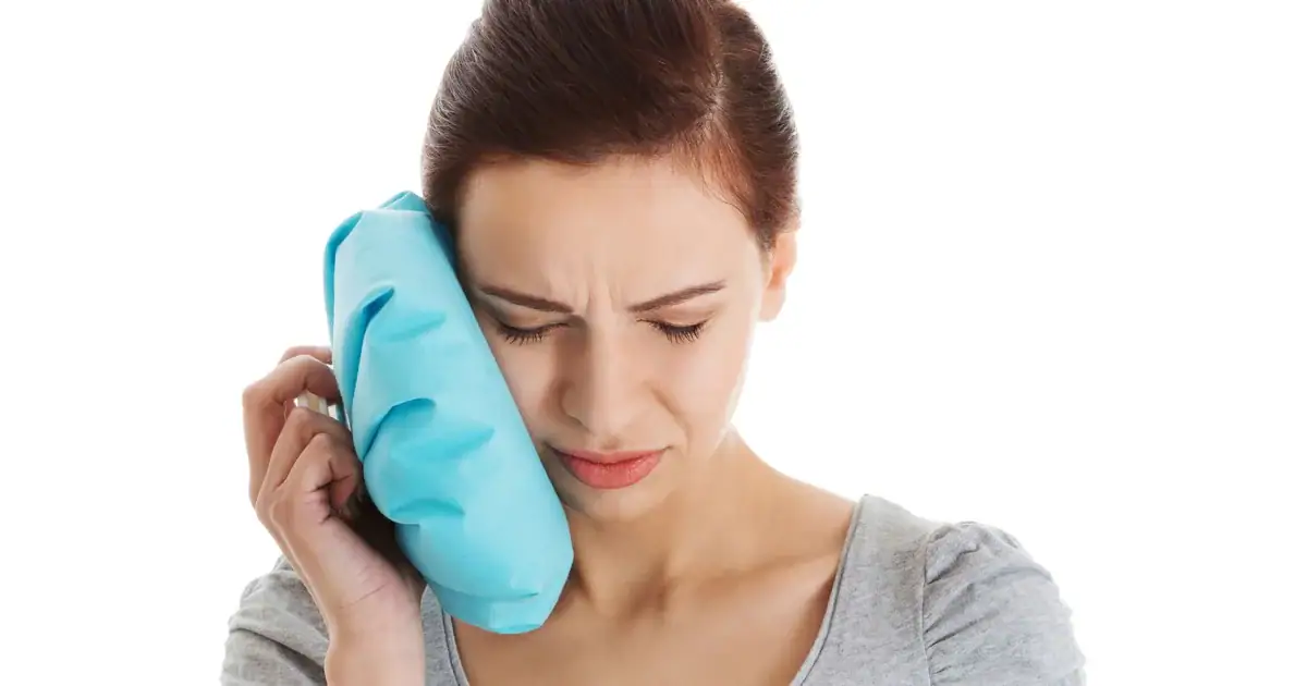 Person applying a cold compress to their cheek in Cardiff